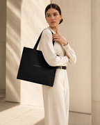 Model carrying XEMORIX XMRX-035 black signature tote bag with centered logo on clean luxury background