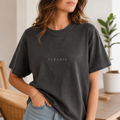 Female model wearing the XEMORIX Signature T-Shirt in Pepper Black with centered chest wordmark in a premium indoor lifestyle setting
