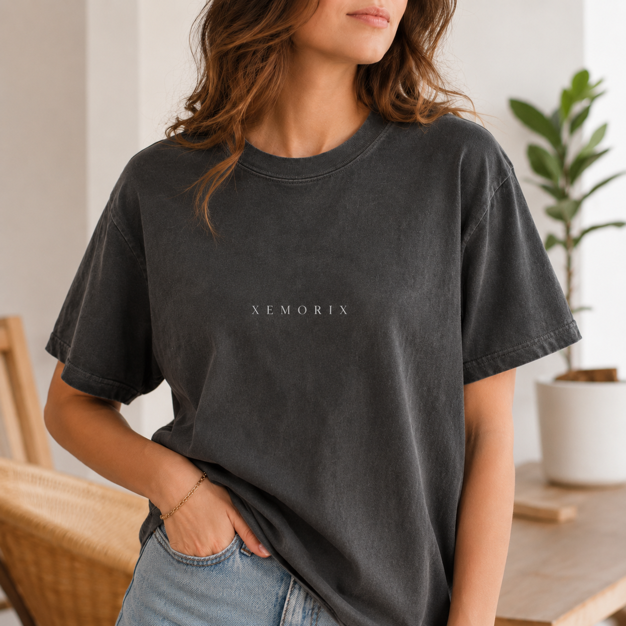 Female model wearing the XEMORIX Signature T-Shirt in Pepper Black with centered chest wordmark in a premium indoor lifestyle setting