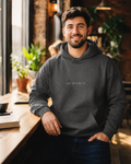 Male model wearing the XEMORIX XMRX-020 Signature Hoodie in Charcoal Heather with centered chest wordmark in a premium lifestyle setting