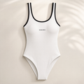 White XEMORIX one-piece swimsuit with black trim and centered logo, styled in a clean luxury resort look.